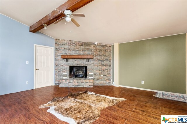 unfurnished living room with brick wall, ceiling fan, hardwood / wood-style floors, vaulted ceiling with beams, and a wood stove