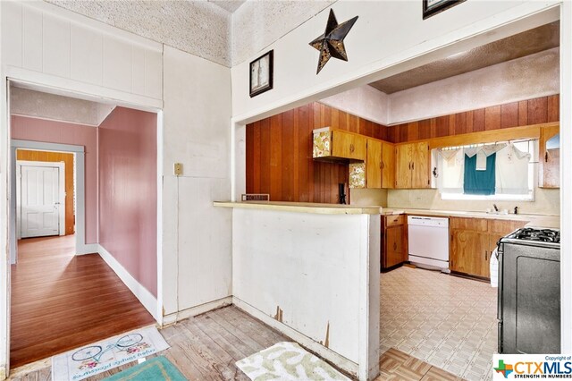 kitchen featuring black stove, a textured ceiling, white dishwasher, wood walls, and light hardwood / wood-style floors