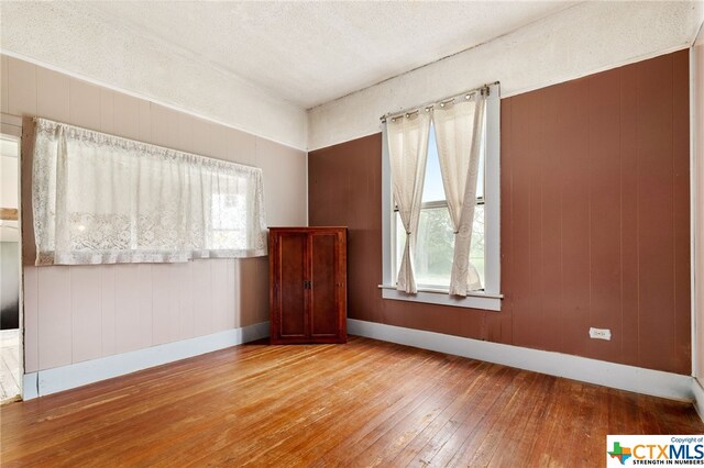 spare room with wood walls, a textured ceiling, a healthy amount of sunlight, and light hardwood / wood-style flooring