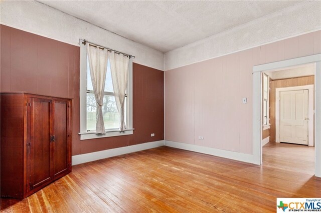 empty room featuring light hardwood / wood-style floors, a textured ceiling, and wooden walls