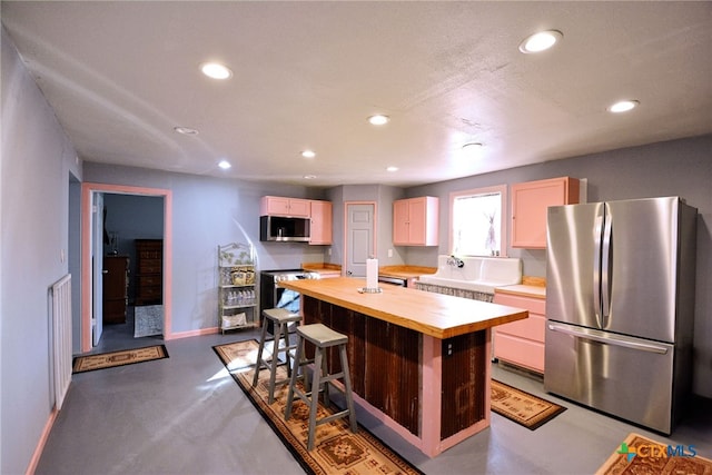 kitchen featuring concrete flooring, a breakfast bar, butcher block counters, a center island, and appliances with stainless steel finishes