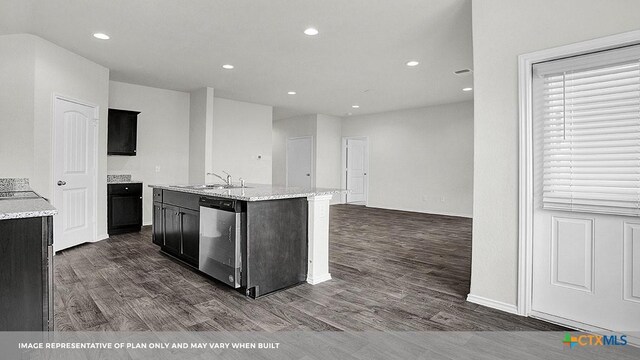 kitchen with light stone countertops, dishwasher, sink, dark wood-type flooring, and a center island with sink