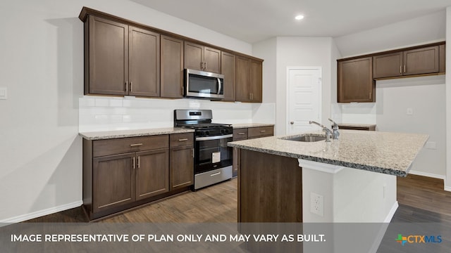 kitchen featuring appliances with stainless steel finishes, an island with sink, sink, dark brown cabinets, and dark wood-type flooring