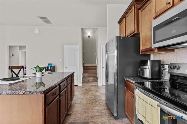 6203 Morganite Dr, Killeen, TX 76542 - kitchen with appliances with stainless steel finishes, dark stone counters, brown cabinets, decorative backsplash, and a kitchen island