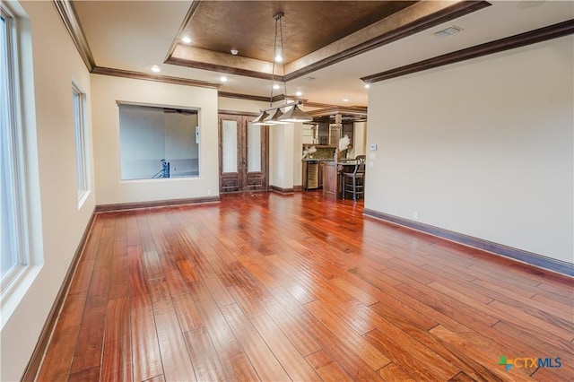 unfurnished living room with ornamental molding, wood-type flooring, and a raised ceiling