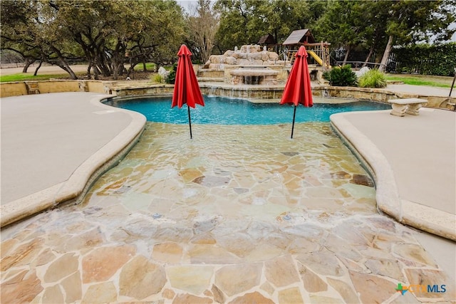 view of pool featuring a patio area, pool water feature, and a playground