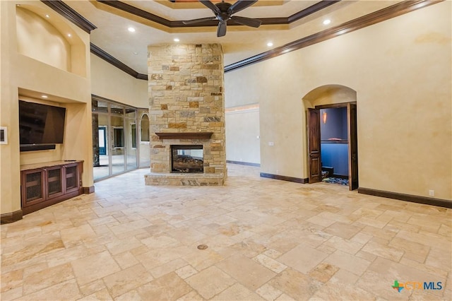 unfurnished living room featuring a towering ceiling, a stone fireplace, ornamental molding, and ceiling fan