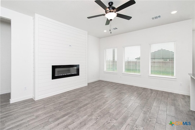 unfurnished living room with ceiling fan, a large fireplace, and light hardwood / wood-style floors