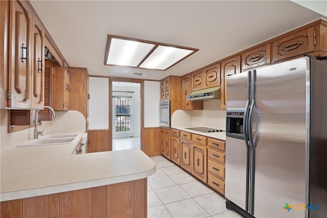 kitchen with wood walls, kitchen peninsula, sink, light tile patterned flooring, and appliances with stainless steel finishes