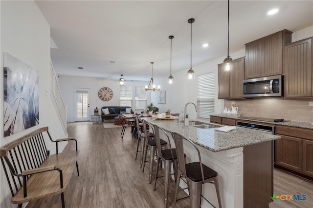 kitchen with sink, light hardwood / wood-style floors, pendant lighting, a center island with sink, and appliances with stainless steel finishes