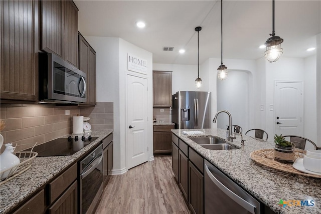 kitchen with sink, stainless steel appliances, light stone counters, pendant lighting, and light wood-type flooring