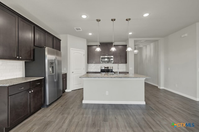 kitchen with pendant lighting, a center island with sink, hardwood / wood-style flooring, tasteful backsplash, and stainless steel appliances