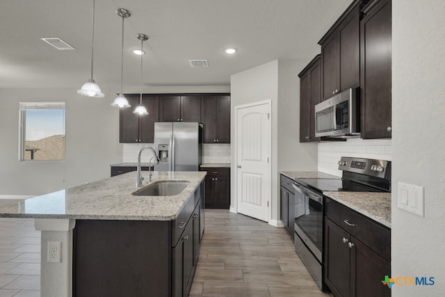 kitchen with tasteful backsplash, stainless steel appliances, a kitchen island with sink, sink, and pendant lighting