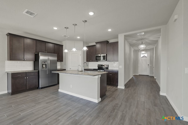 kitchen featuring pendant lighting, backsplash, a kitchen island with sink, light wood-type flooring, and appliances with stainless steel finishes