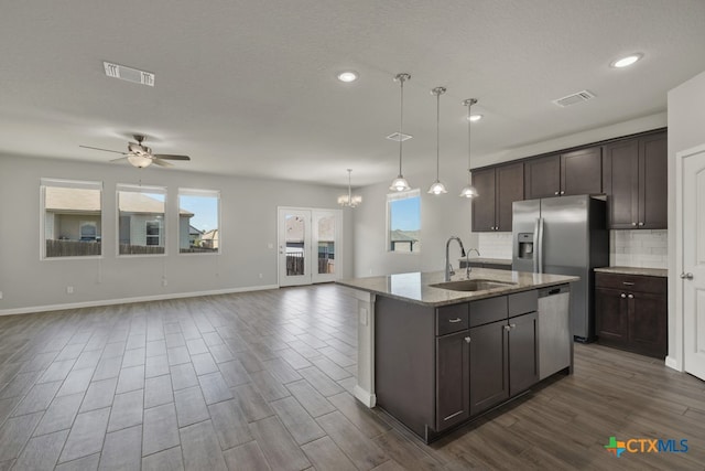 kitchen featuring sink, hanging light fixtures, appliances with stainless steel finishes, light stone countertops, and a kitchen island with sink