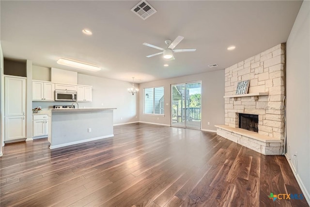 unfurnished living room with dark wood-type flooring, a stone fireplace, and ceiling fan with notable chandelier