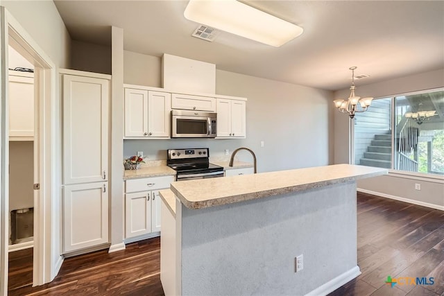 kitchen featuring white cabinetry, appliances with stainless steel finishes, decorative light fixtures, and a center island with sink