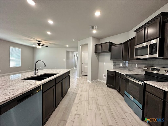 kitchen featuring sink, ceiling fan, stainless steel appliances, light stone counters, and tasteful backsplash