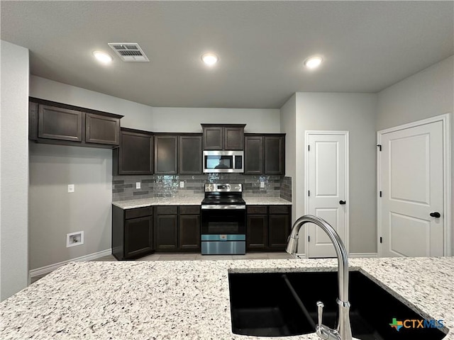 kitchen with light stone counters, appliances with stainless steel finishes, sink, and backsplash