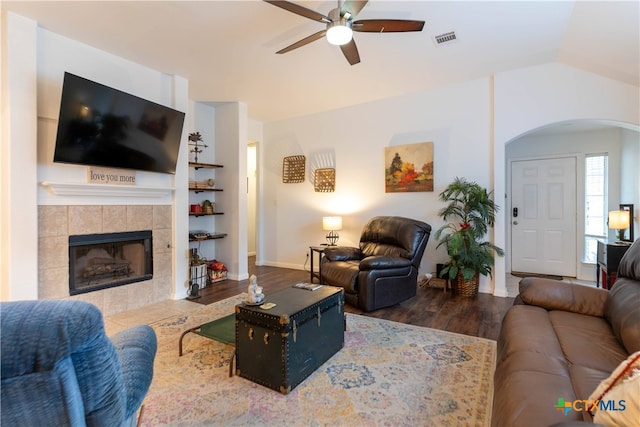 living room featuring built in features, a tiled fireplace, hardwood / wood-style flooring, lofted ceiling, and ceiling fan