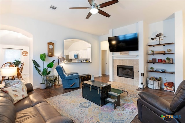 living room featuring dark wood-type flooring, ceiling fan, and a fireplace