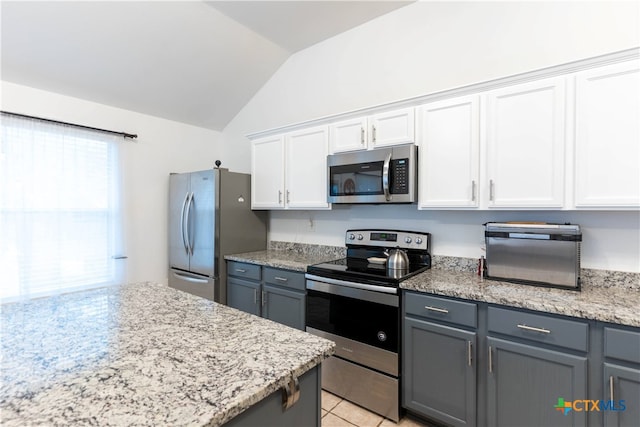 kitchen with stainless steel appliances, light stone counters, light tile patterned floors, white cabinets, and vaulted ceiling