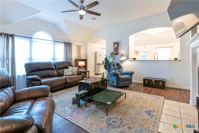 living room with dark wood-type flooring, ceiling fan, a fireplace, and lofted ceiling