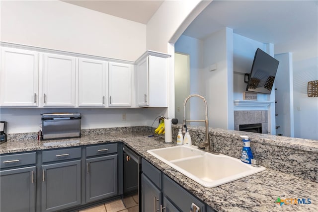 kitchen featuring dishwasher, a tiled fireplace, sink, and white cabinets