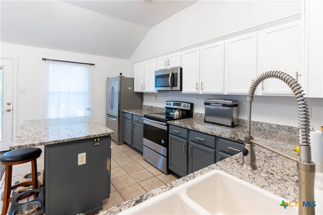 kitchen with a kitchen bar, stainless steel appliances, vaulted ceiling, light tile patterned floors, and white cabinetry