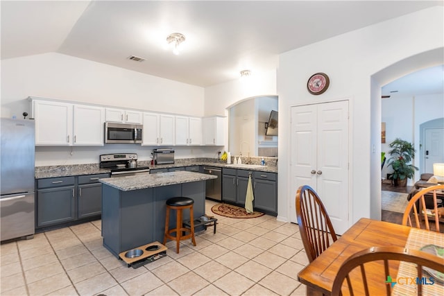 kitchen with white cabinetry, appliances with stainless steel finishes, light tile patterned floors, vaulted ceiling, and a center island