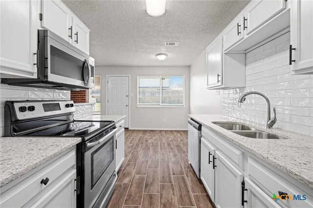 kitchen with wood finish floors, a sink, backsplash, stainless steel appliances, and white cabinets