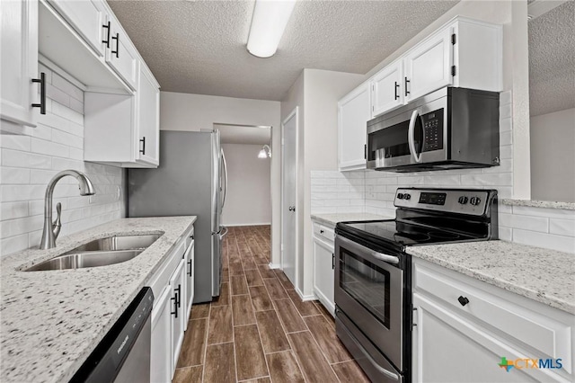 kitchen with light stone counters, wood tiled floor, a sink, stainless steel appliances, and white cabinets