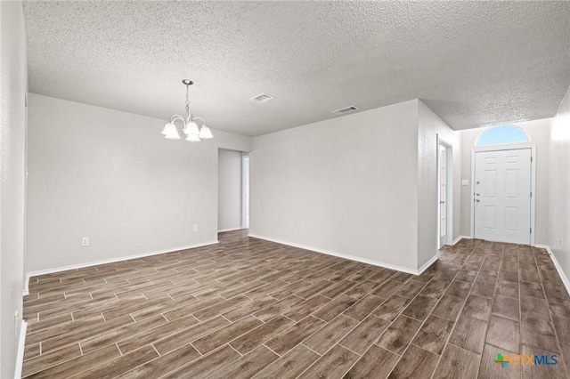 spare room featuring a notable chandelier, baseboards, dark wood-type flooring, and visible vents