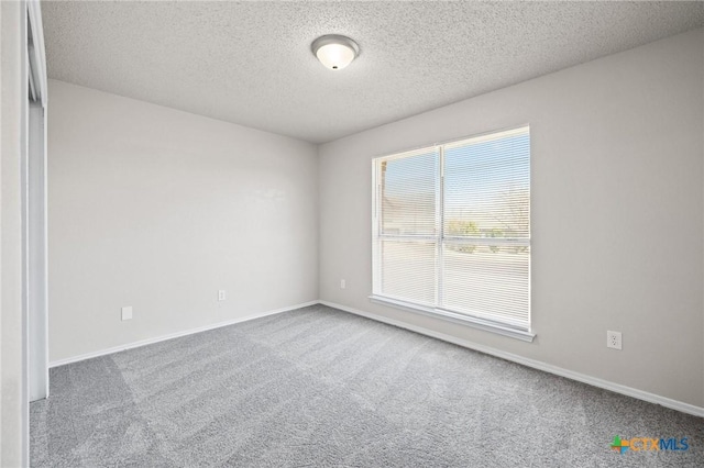 carpeted spare room with a textured ceiling and baseboards