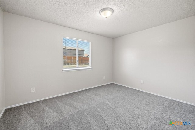 carpeted spare room featuring a textured ceiling and baseboards