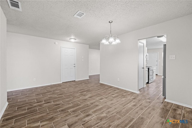 unfurnished room featuring wood finish floors, visible vents, baseboards, and an inviting chandelier