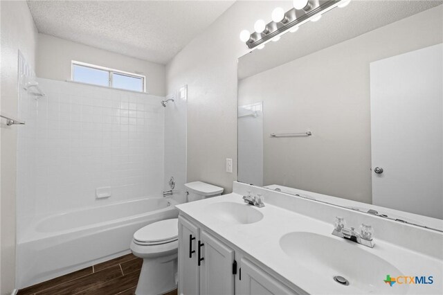 full bathroom featuring a textured ceiling, wood finish floors, toilet, and a sink