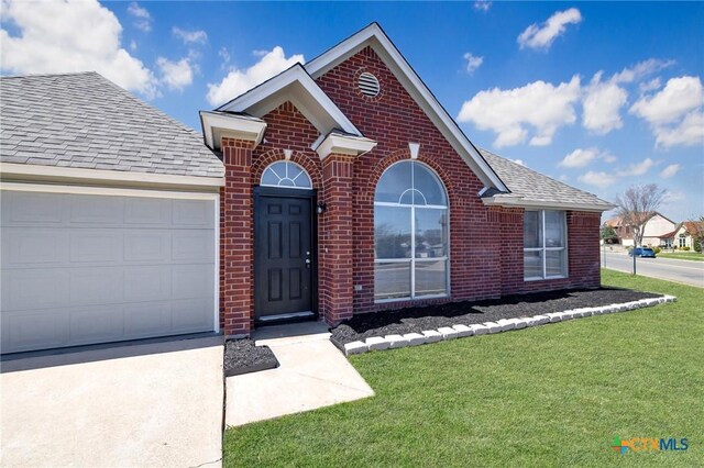 view of front facade with a shingled roof, concrete driveway, a front yard, an attached garage, and brick siding