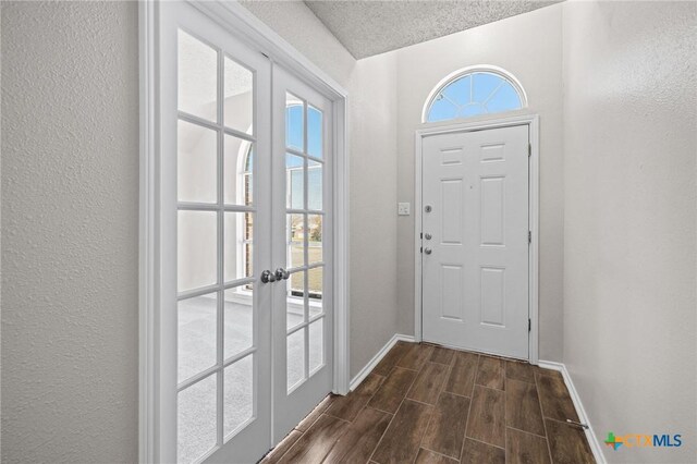 doorway to outside with baseboards, wood finish floors, french doors, a textured wall, and a textured ceiling