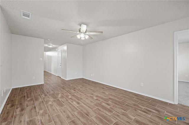 empty room with wood finished floors, baseboards, a ceiling fan, visible vents, and a textured ceiling