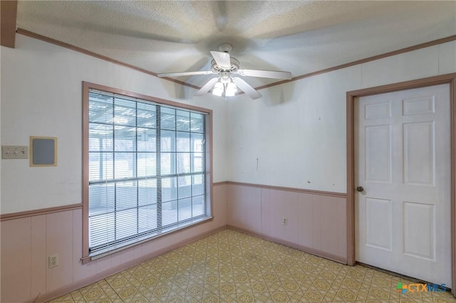 unfurnished room with a wainscoted wall, crown molding, and a textured ceiling