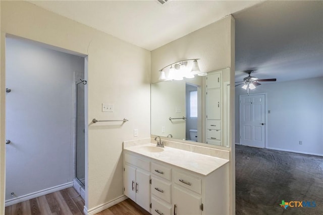 full bath featuring baseboards, ceiling fan, wood finished floors, a shower with shower door, and vanity