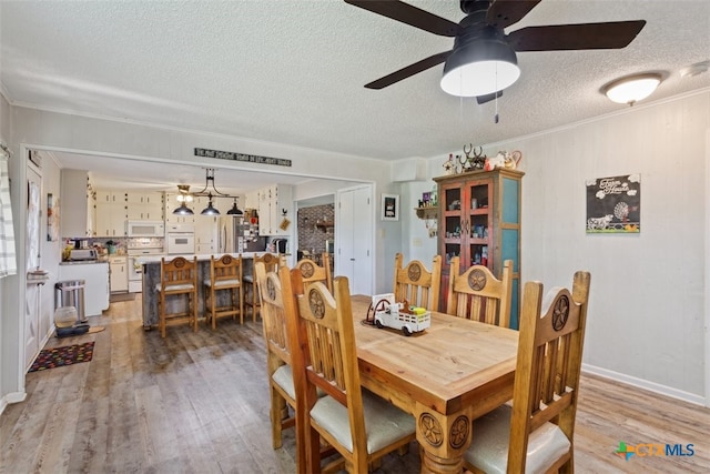 dining space with ceiling fan, a textured ceiling, light wood-type flooring, and ornamental molding