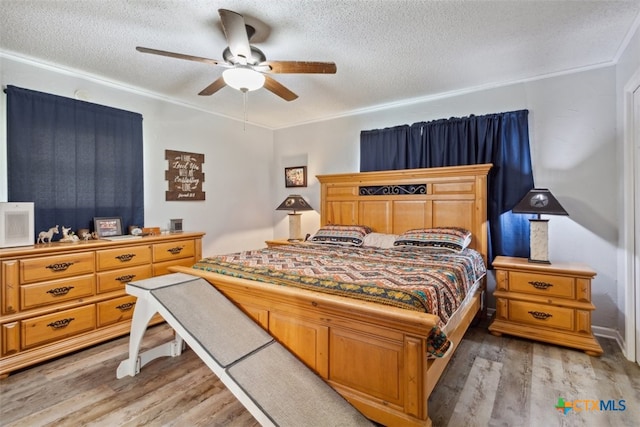 bedroom featuring ceiling fan, a textured ceiling, light wood-type flooring, and ornamental molding