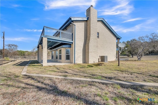 view of home's exterior with brick siding, a yard, a chimney, central AC unit, and a patio area