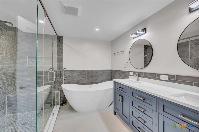 full bathroom with double vanity, visible vents, a freestanding bath, a shower stall, and a sink