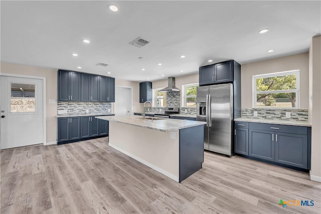 kitchen with stainless steel appliances, visible vents, a sink, wall chimney range hood, and an island with sink