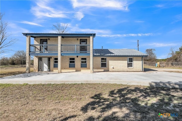 back of property featuring brick siding, metal roof, and a balcony