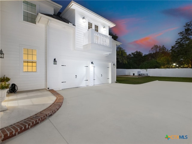 property exterior at dusk with a balcony, concrete driveway, a garage, and metal roof