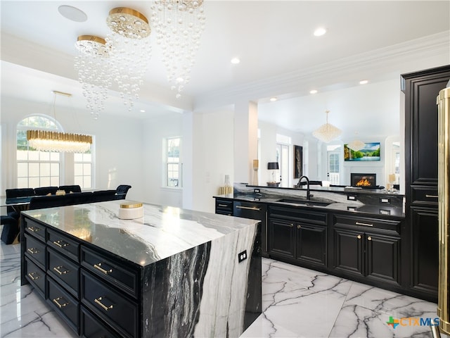 kitchen with marble finish floor, a sink, a warm lit fireplace, dark cabinetry, and crown molding